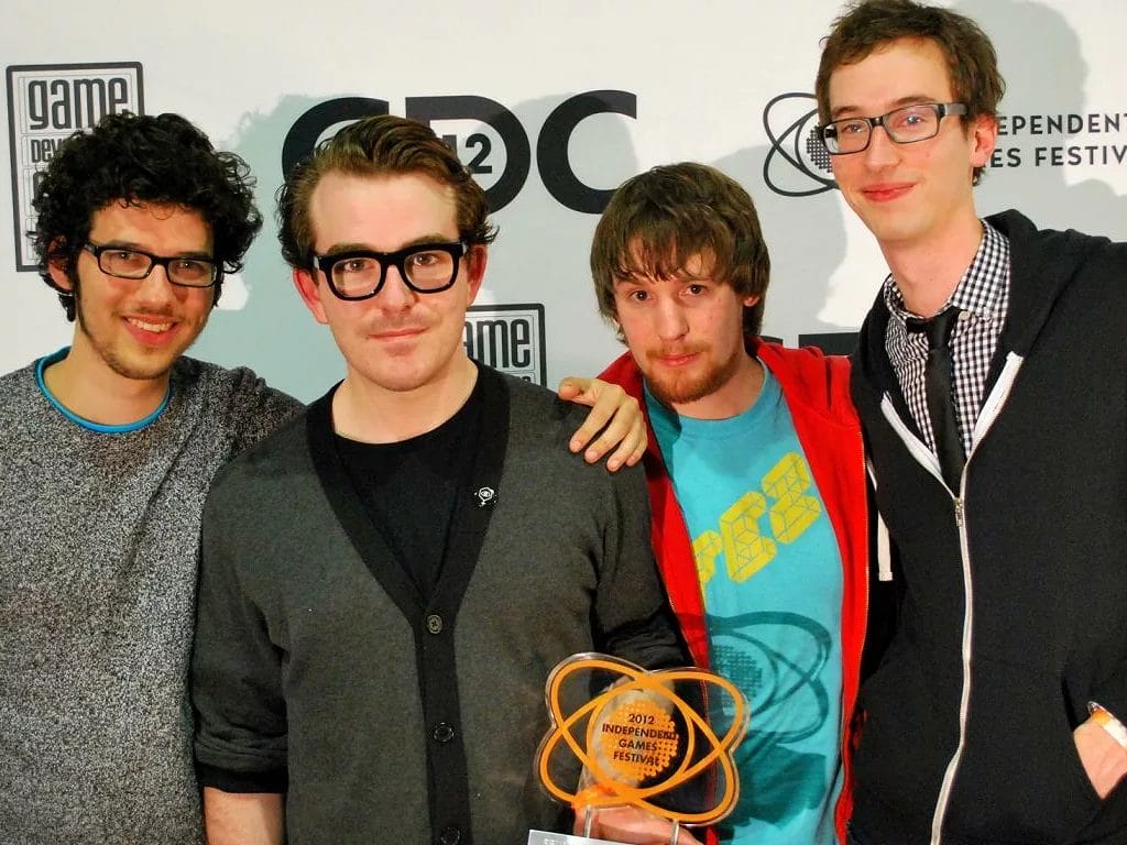 A group of young men posing for a picture with an award while discussing indie game development.