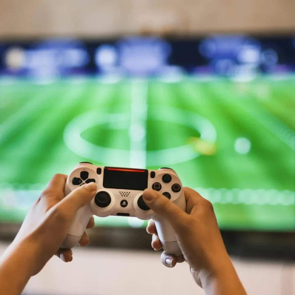  Game developers: don't make these top 3 mistakes - Playing games - Photo by EVG Kowalievska on Pexels.com Person holding a video game controller in front of a TV screen displaying a soccer video game—a perfect reminder for game developers: don't make these top 4 mistakes when designing immersive sports experiences.